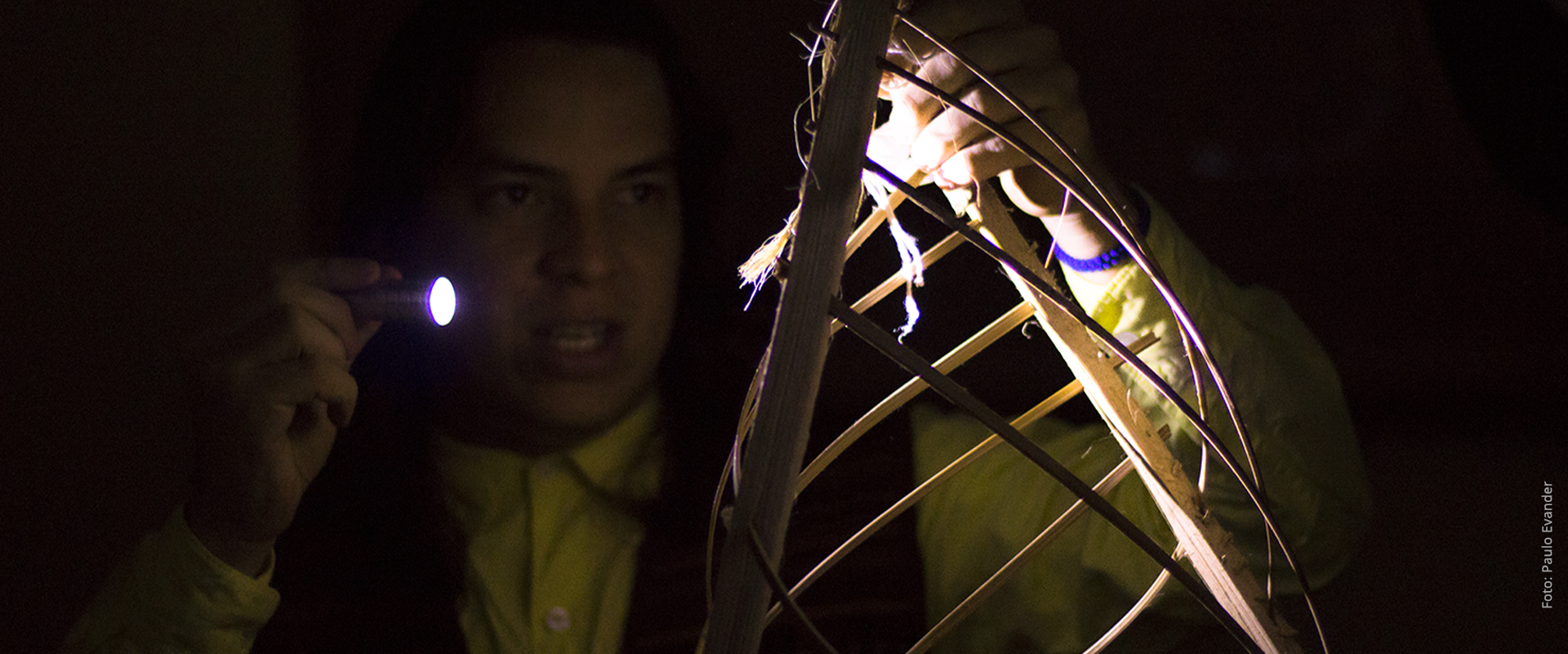 Fotografia da performance "731 são doze", um ator segura uma lanterna que ilumina objeto feito de miriti